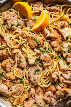 a skillet filled with pasta, meat and lemon wedges