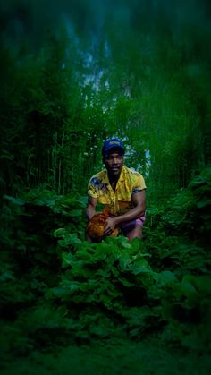 a man kneeling down in the middle of a forest holding a chicken and wearing a helmet