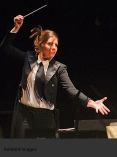 a woman in a suit and tie holding a conductor's baton with both hands