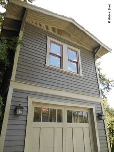 a gray house with two windows on the top floor and one window above the garage door