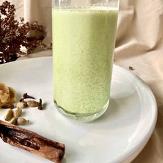 a glass filled with green liquid sitting on top of a white plate next to nuts