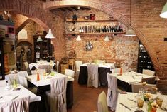 a restaurant with tables and chairs covered in white tablecloths, wine bottles on the wall