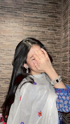 a woman covering her face with her hands while standing in front of a brick wall