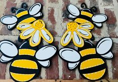 two wooden bees with yellow and white designs on them, one has a flower in the middle