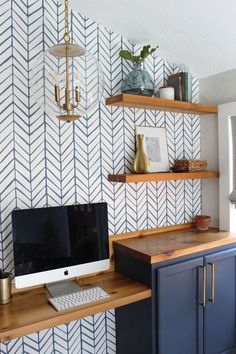 a desk with a computer on it in front of a wallpapered wall and shelves