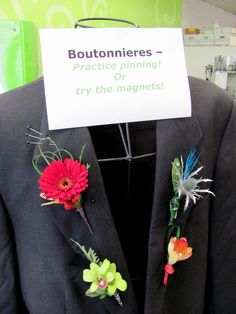 a suit jacket with flowers pinned to it's lapel, and a sign that says boutonnieres practice winning try the magnets