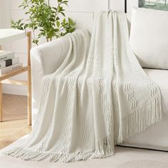 a white couch with a blanket on top of it next to a potted plant