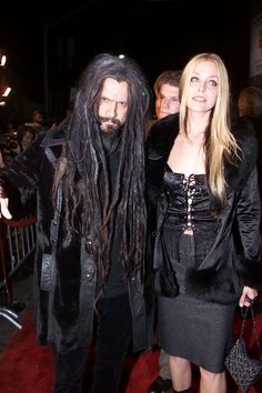 a man with long hair standing next to a woman in a black dress on a red carpet