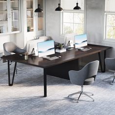 an office desk with two computers on it in front of three large windows and some chairs