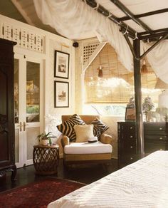 a bed sitting under a canopy next to a chair and dresser in a room with pictures on the wall