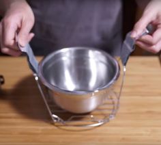 a person holding a metal bowl on top of a wooden table with utensils