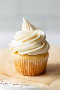 a cupcake with white frosting sitting on top of a piece of parchment paper