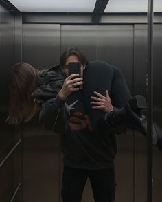 a man taking a selfie with his cell phone in an elevator while another person takes a photo