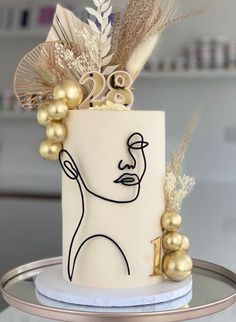 a white cake with gold decorations and feathers on it's head is sitting on a table