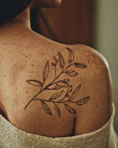 the back of a woman's shoulder with an olive branch and bird tattoo on it