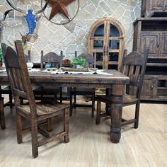 a rustic dining table and chairs in front of a stone wall