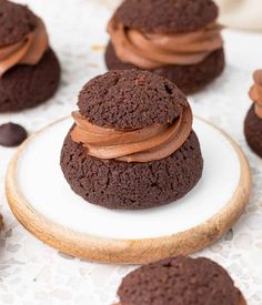 chocolate cookies with peanut butter frosting on a white and wooden plate next to other cookies