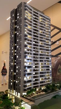 a model of a tall building with lights on it's sides and people in the background