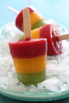 two popsicles are on top of ice and one is red, yellow and green