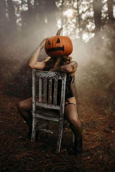 a woman sitting on top of a wooden chair holding a pumpkin in her hands and covering her face