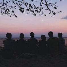 four people sitting on the beach watching the sunset