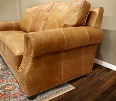 a tan leather couch sitting on top of a wooden floor next to a rug and wall