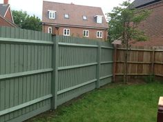 a wooden fence in front of a brick building and green grass with a bench next to it