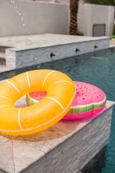 two inflatable watermelon floats sitting on the edge of a swimming pool