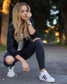 a woman squatting on the ground with her hand near her face and looking at the camera