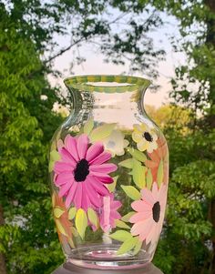 a vase with flowers painted on it sitting on a table in front of some trees