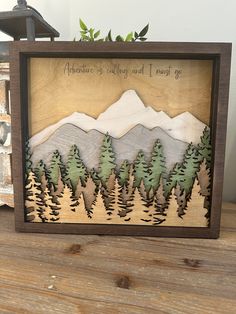 a wooden frame with some trees and mountains in the background on top of a table