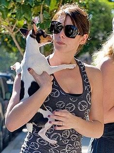 two women walking down the street with a dog on their shoulders and one woman holding a small dog in her arms