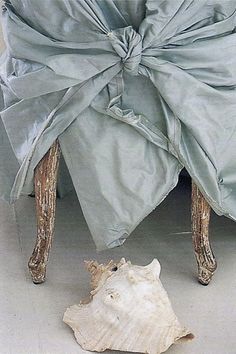 an upholstered chair covered in a blue cloth with a seashell on the floor