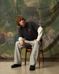 a young man sitting on top of a chair in front of a wall with paintings