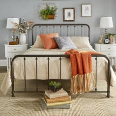 a bedroom with a metal bed frame and orange throw pillows on top of the bed