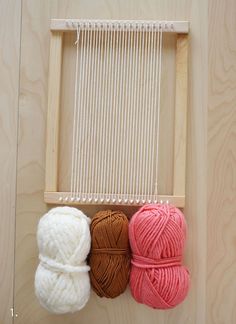 three balls of yarn sitting on top of a wooden frame next to a ball of yarn