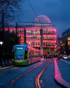 a train on the tracks in front of a large building with neon lights at night