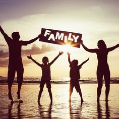 four people holding up a family sign on the beach at sunset with their arms in the air