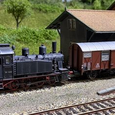 a toy train is on the tracks next to a small building and trees in the background