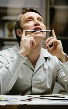 a man sitting at a desk holding a pen in his mouth and looking up to the sky