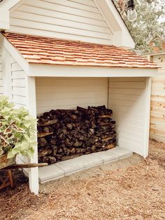 a pile of logs sitting in front of a white building with a red roof and brown shingles