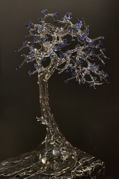 a clear glass tree with blue flowers in it's branches on a black background