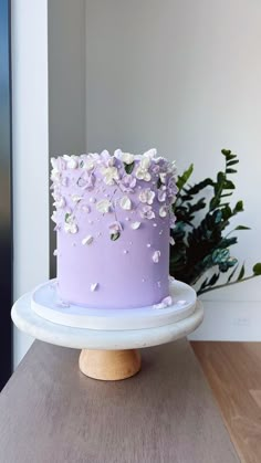 a purple cake sitting on top of a wooden table next to a potted plant