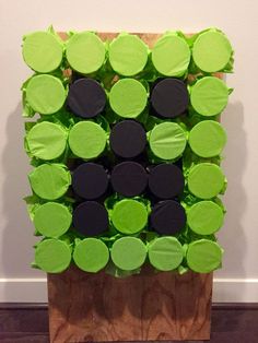 an art piece made out of green and black circles on a wooden block in front of a white wall