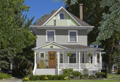 a white house with green trim and trees in the front yard, on a sunny day