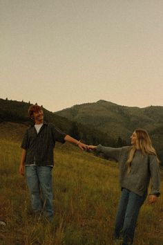 two people holding hands while standing in a field