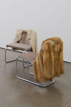 two chairs with furs on them in an empty room and one chair has a footstool