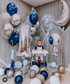 a baby sitting at a table surrounded by balloons