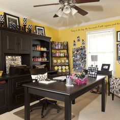 an office with yellow walls and black desk in the center is decorated with lots of pictures