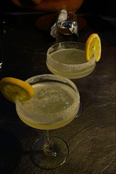 two margaritas sitting on top of a table with lemon wedged in the rim